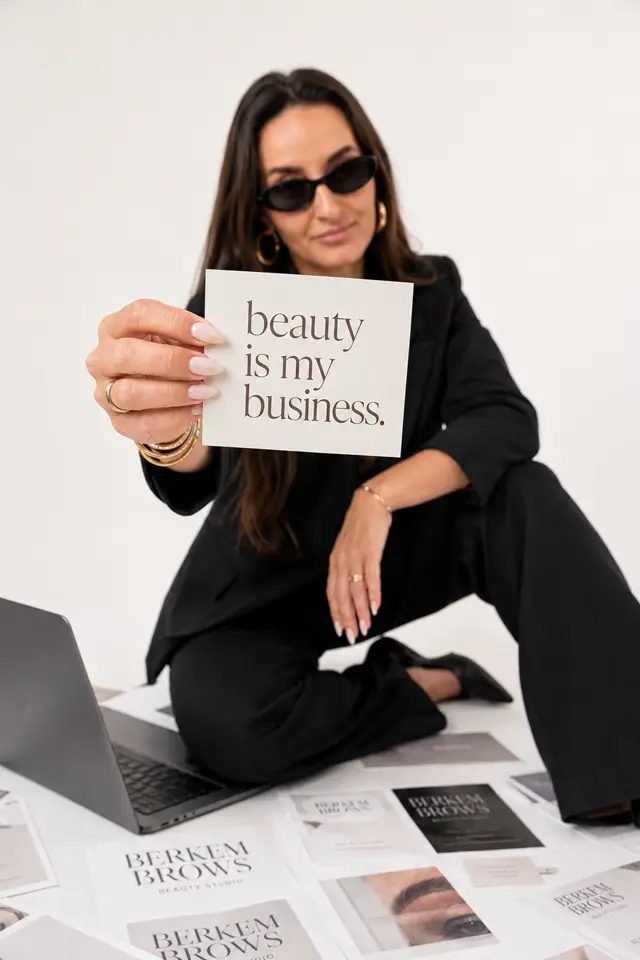 Kellen at a desk with a laptop and a card that reads beauty is my business